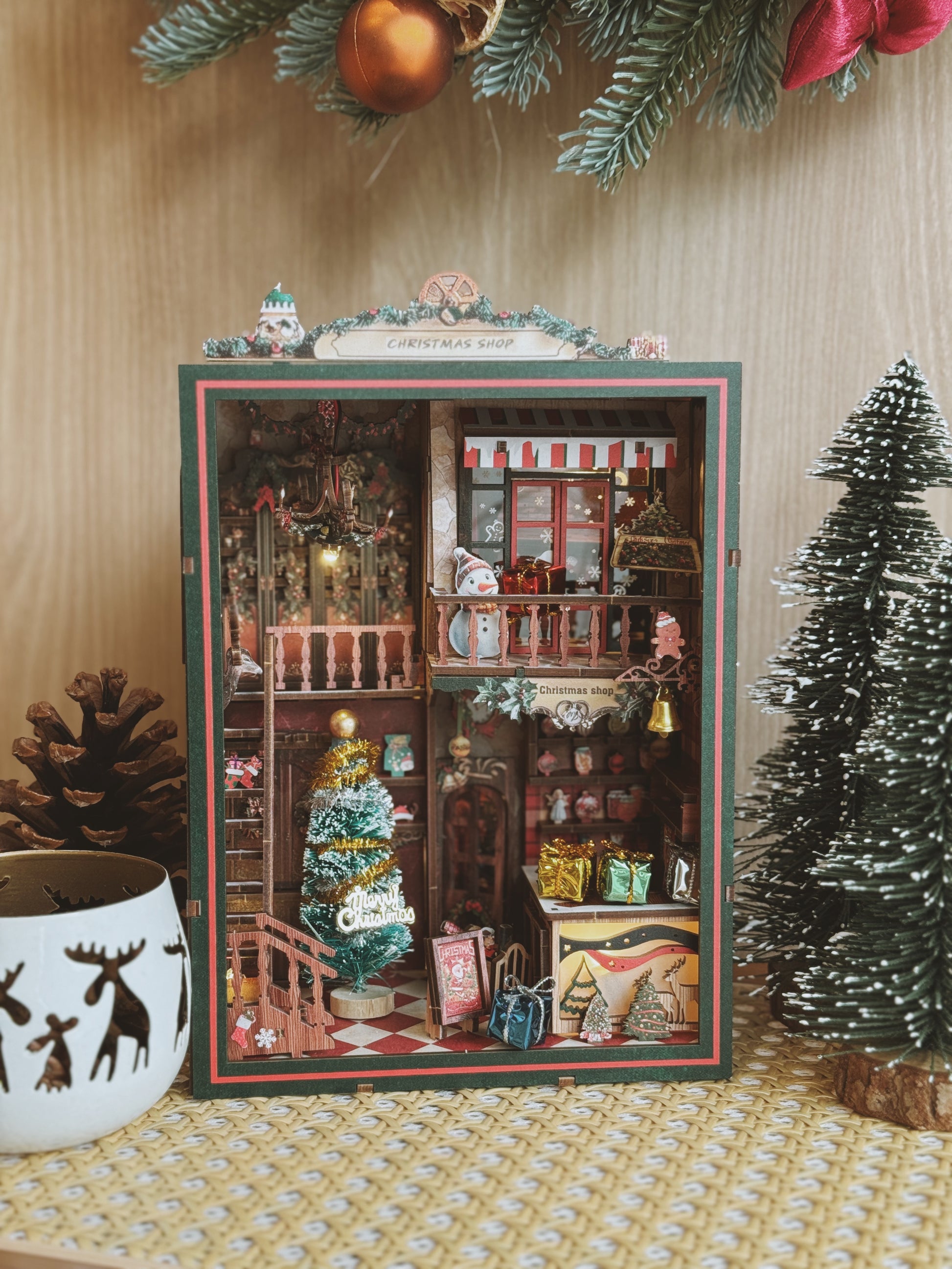 Miniature dollhouse scene inside a decorated box with Christmas decorations around