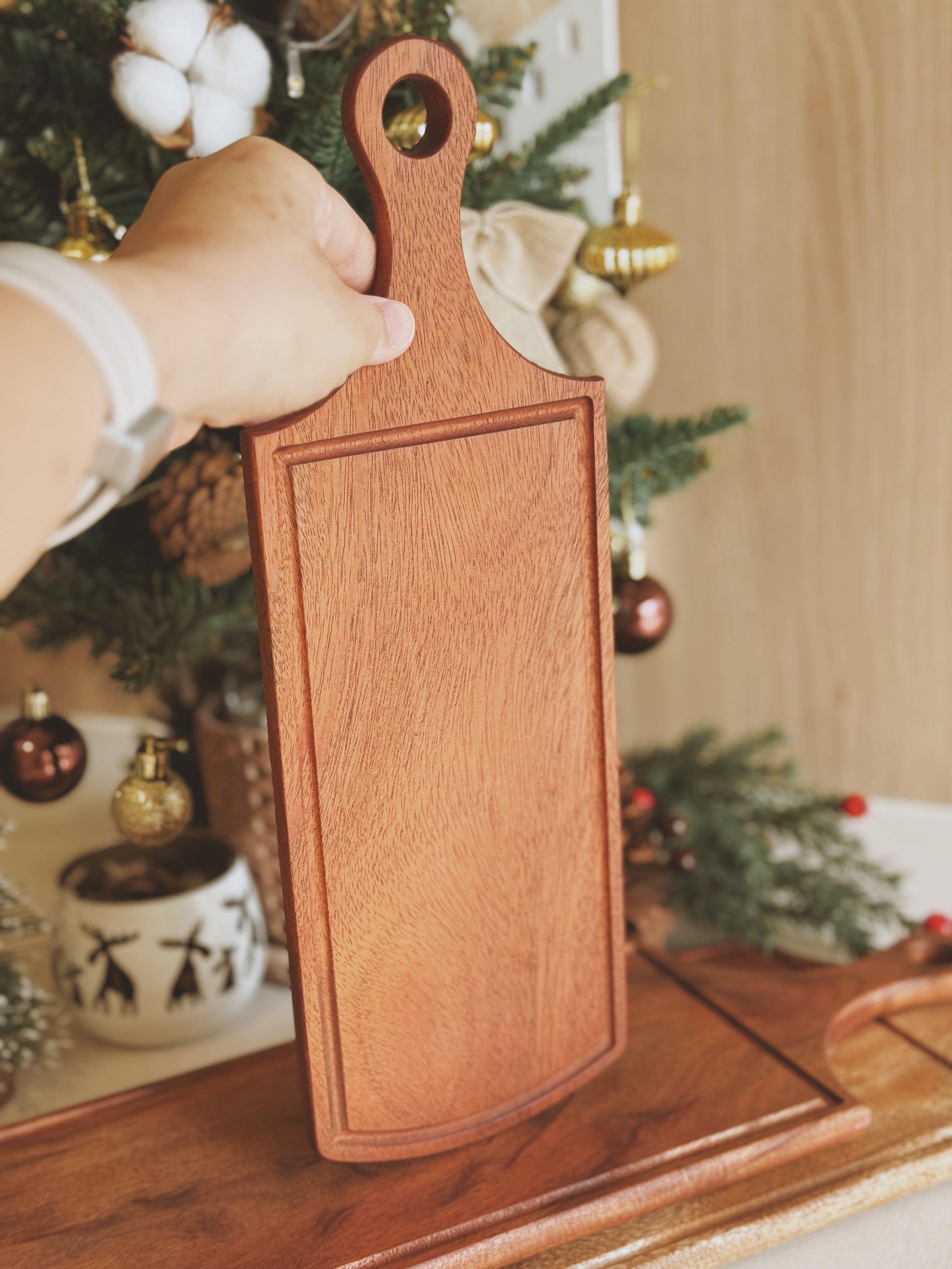 Wooden cutting board held by a hand with a Christmas tree in the background