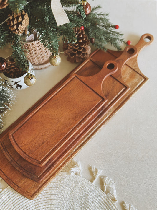 Wooden cutting board on a surface with a Christmas tree in the background